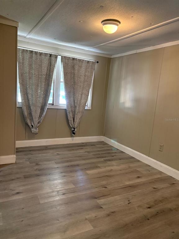 An empty room features light wood-look flooring, beige paneled walls, and a window with curtains — 1616 TERRY ROAD, LAKELAND, FL