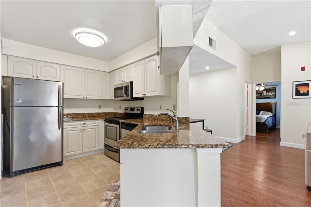 A kitchen with white cabinets, stainless steel appliances, and granite countertops overlooks a living area — 2550 N ALAFAYA TRAIL UNIT 11206, ORLANDO, FL