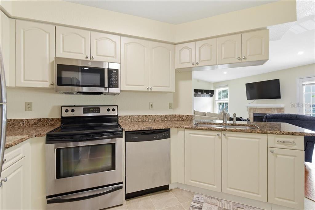 A kitchen features cream-colored cabinets, granite countertops, and stainless steel appliances — 2550 N ALAFAYA TRAIL UNIT 11206, ORLANDO, FL