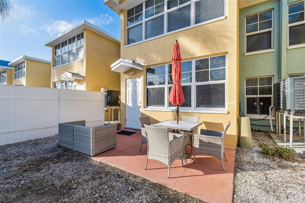 A patio with a table, chairs, and an umbrella sits outside a yellow townhouse — 19417 GULF BOULEVARD UNIT F107, INDIAN ROCKS BEACH, FL