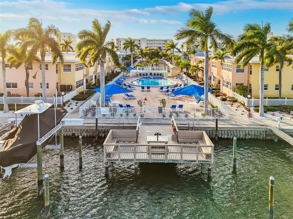 An aerial view of a waterfront pool area with palm trees, lounge chairs, and a dock — 19417 GULF BOULEVARD UNIT F107, INDIAN ROCKS BEACH, FL