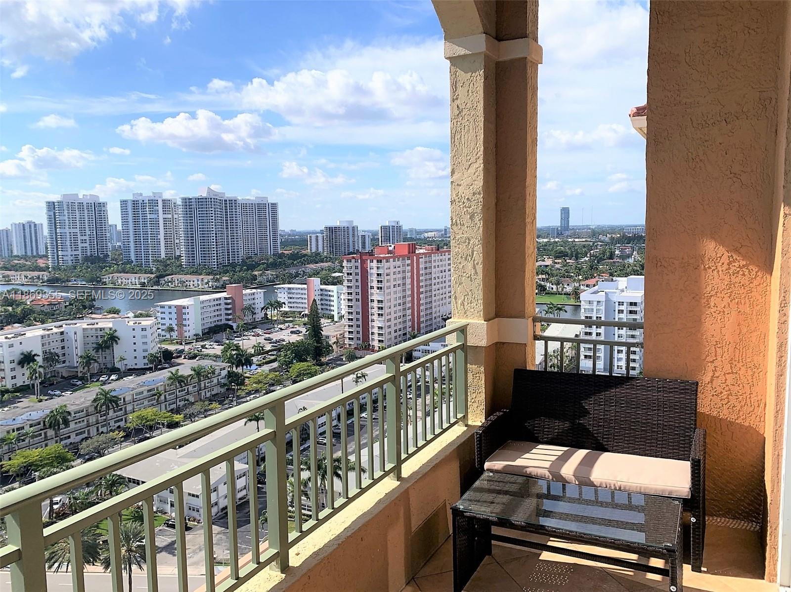 A balcony with a wicker bench and glass table overlooks a city skyline and water — 2080 S OCEAN DRIVE, Hallandale Beach FL 33009, HALLANDALE BEACH, FL