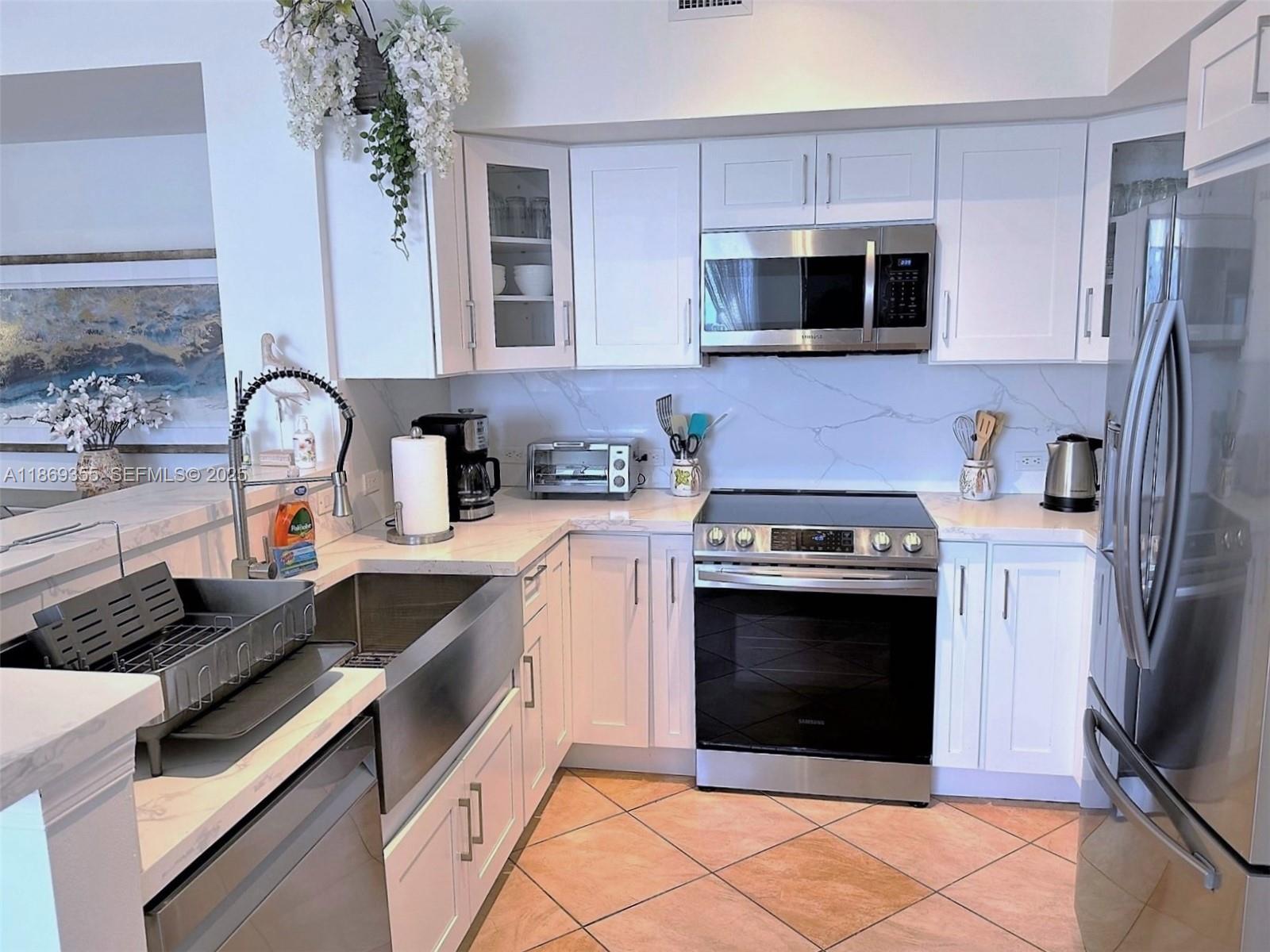 A kitchen features white cabinets, stainless steel appliances, a farmhouse sink, and marble-patterned countertops — 2080 S OCEAN DRIVE, Hallandale Beach FL 33009, HALLANDALE BEACH, FL