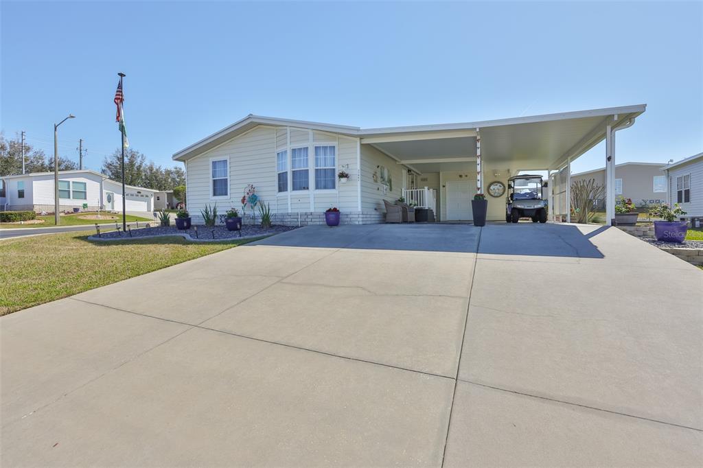 A light-colored manufactured home features a concrete driveway, a carport, and a small front garden — 37041 NEUKOM AVENUE, ZEPHYRHILLS, FL