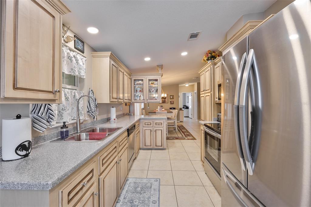 A kitchen features light wood cabinets, granite countertops, stainless steel appliances, and tile flooring — 37041 NEUKOM AVENUE, ZEPHYRHILLS, FL