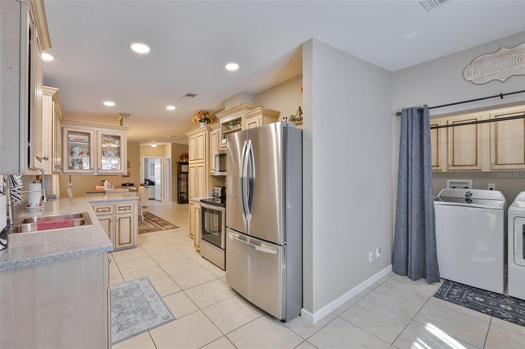 A kitchen with light-colored cabinets, stainless steel appliances, and an adjacent laundry area — 37041 NEUKOM AVENUE, ZEPHYRHILLS, FL