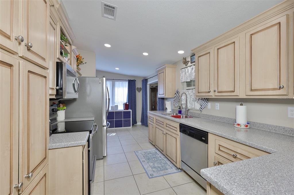 A kitchen features light wood cabinets, granite countertops, stainless steel appliances, and tile flooring — 37041 NEUKOM AVENUE, ZEPHYRHILLS, FL
