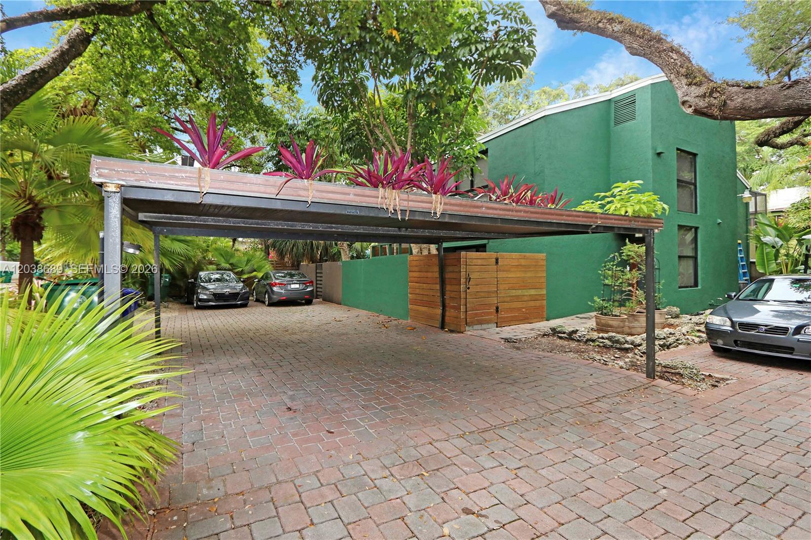 A paved driveway features a metal carport with potted plants on top next to a building — 3138 Mary St # 3138, Miami FL 33133, MIAMI, FL