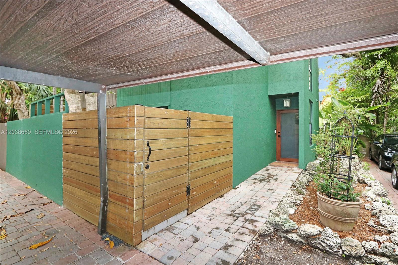 A green exterior wall features a wooden privacy fence, a glass door, and brick pavers — 3138 Mary St # 3138, Miami FL 33133, MIAMI, FL