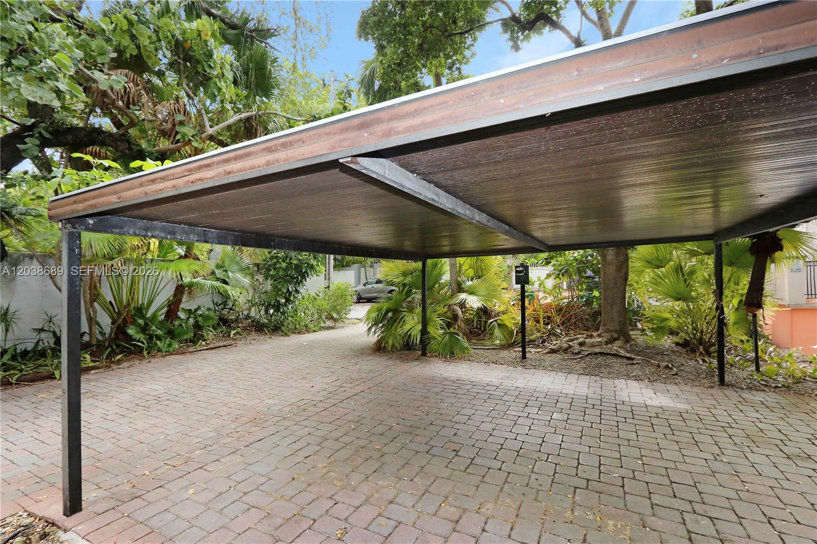 A paved driveway features a metal carport structure surrounded by lush tropical landscaping — 3138 Mary St # 3138, Miami FL 33133, MIAMI, FL