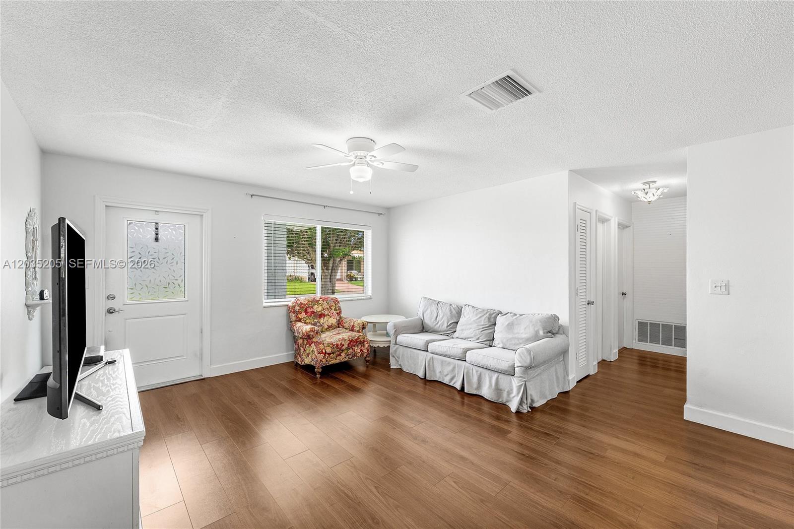 A living room features white walls, wood-look flooring, a floral armchair, and a light-colored sofa — 4705 NW 43rd Ave, Tamarac FL 33319, TAMARAC, FL