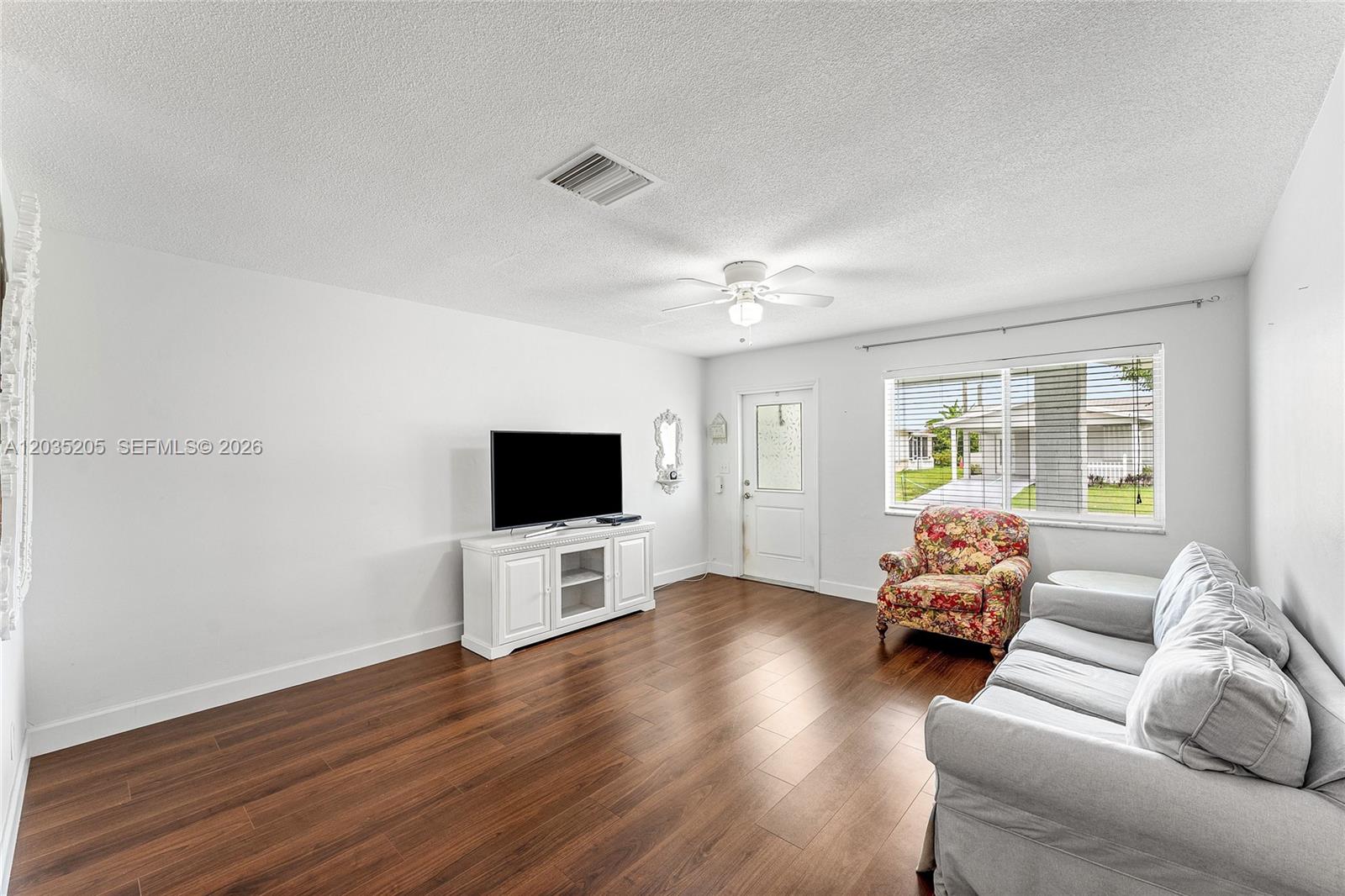 A living room features white walls, dark wood flooring, a television, and a floral chair — 4705 NW 43rd Ave, Tamarac FL 33319, TAMARAC, FL