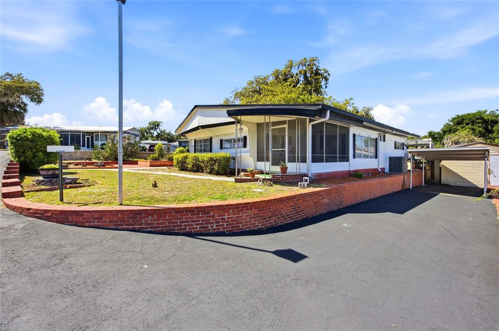 A single-story manufactured home features a screened porch, brick retaining wall, and attached carport — 3896 PICCIOLA ROAD UNIT 411, FRUITLAND PARK, FL