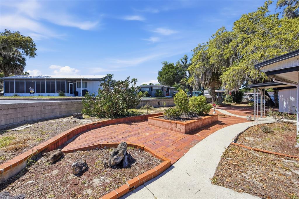 A brick patio with a raised planter bed sits in front of a mobile home — 3896 PICCIOLA ROAD UNIT 411, FRUITLAND PARK, FL