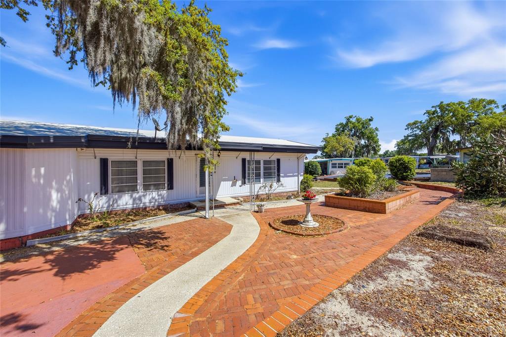 A white mobile home features a brick patio, a birdbath, and a large oak tree — 3896 PICCIOLA ROAD UNIT 411, FRUITLAND PARK, FL