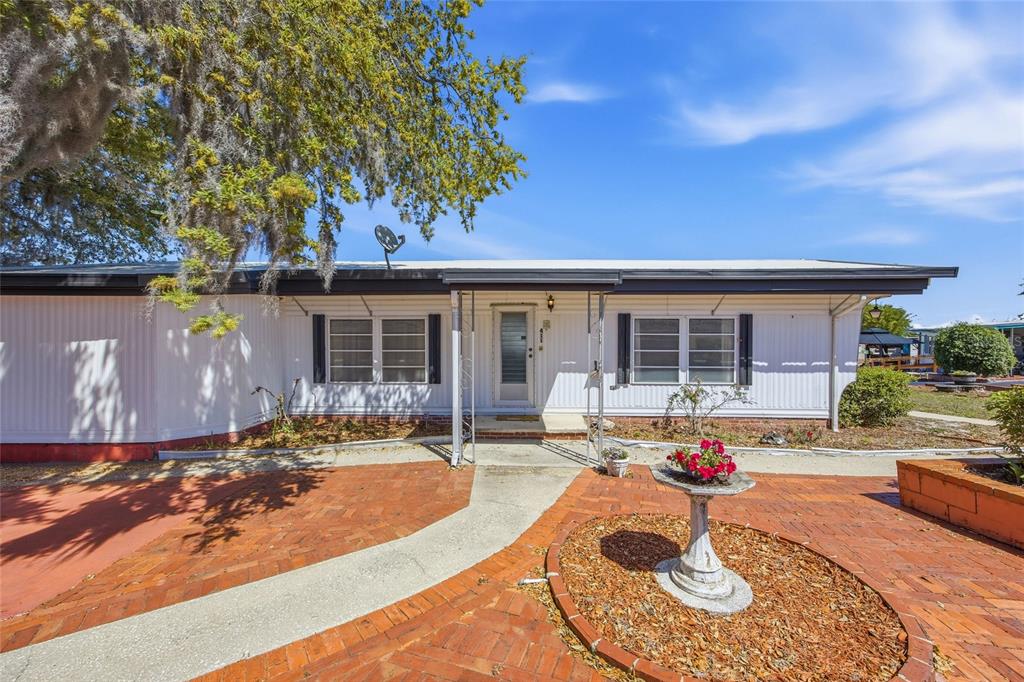 A white mobile home with a brick patio, a birdbath, and a large oak tree — 3896 PICCIOLA ROAD UNIT 411, FRUITLAND PARK, FL