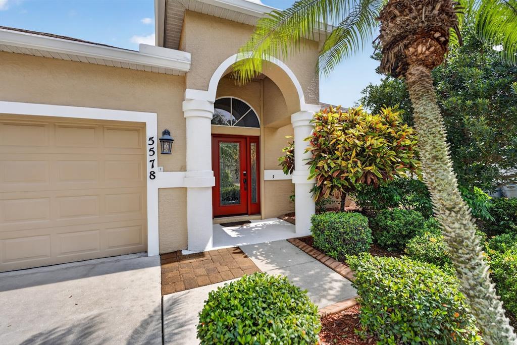 A tan house exterior features a red front door, arched entryway, and a garage — 5578 BURNT BRANCH CIRCLE, SARASOTA, FL