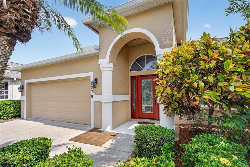 A tan house exterior features a red front door, an arched entryway, and a garage — 5578 BURNT BRANCH CIRCLE, SARASOTA, FL