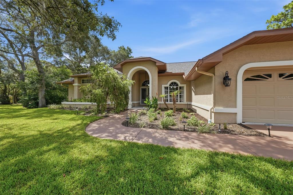 The exterior of a tan house features a curved walkway, arched entryway, and attached garage — 11109 GOLDEN EAGLE AVENUE, WEEKI WACHEE, FL
