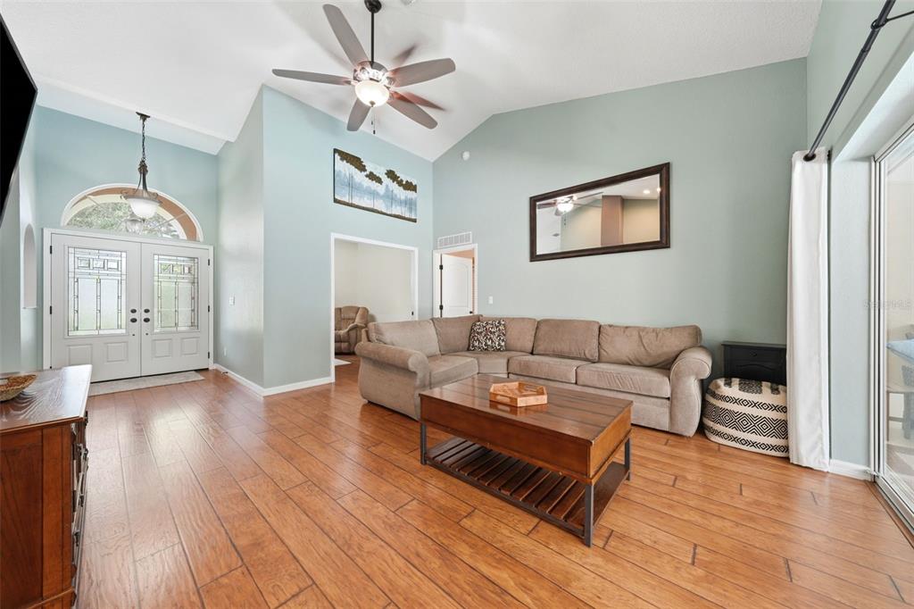 A living room features vaulted ceilings, light blue walls, wood flooring, and a sectional sofa — 11109 GOLDEN EAGLE AVENUE, WEEKI WACHEE, FL
