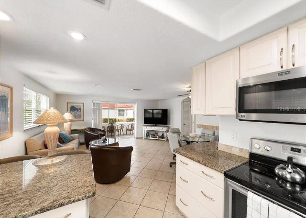 A kitchen with granite countertops and white cabinets overlooks an open-concept living and dining area — 6154 MIDNIGHT PASS ROAD UNIT D18, SARASOTA, FL