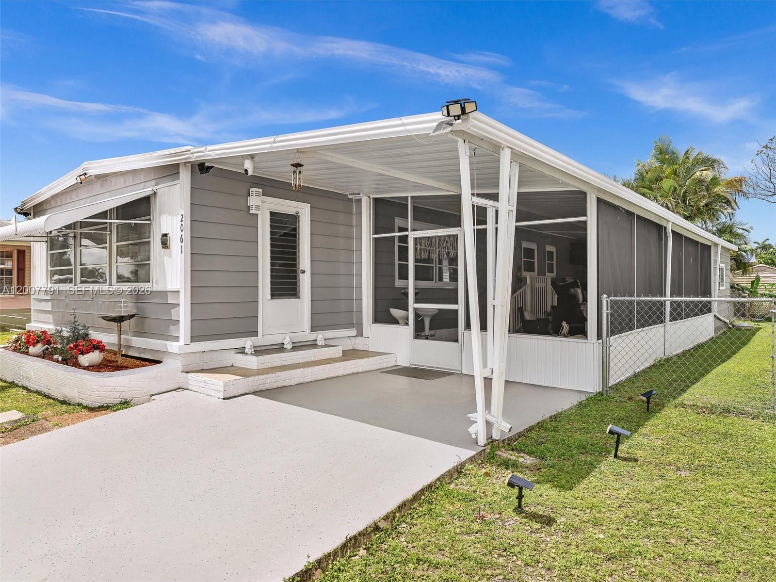 A gray manufactured home features a screened-in porch, a concrete driveway, and a chain-link fence — 2061 SW 83rd Ave, Davie FL 33324, DAVIE, FL