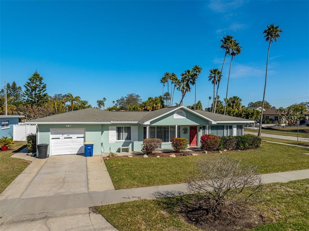 A light green single-story house with a white garage door and palm trees in front — 66 KIPLING PLAZA, CLEARWATER BEACH, FL