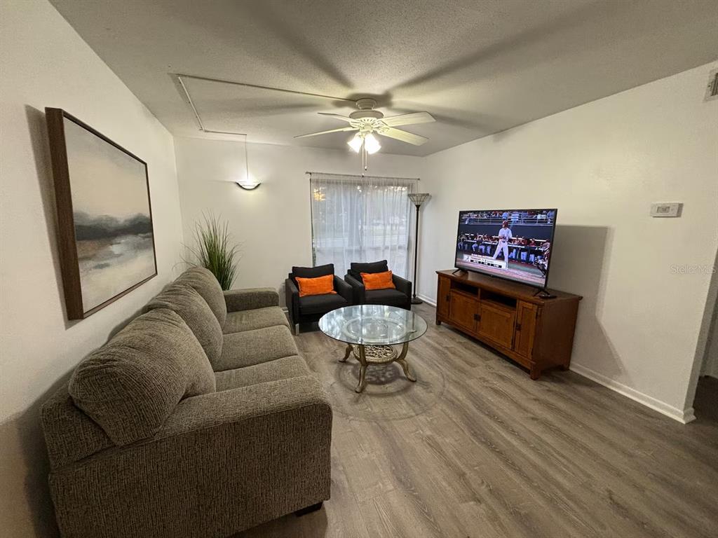 A living room features a gray sofa, two black chairs, a glass coffee table, and television — 1700 SW 16TH COURT UNIT A5, GAINESVILLE, FL