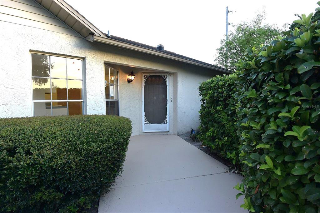 A concrete walkway leads to the front entrance of a house with white stucco siding — 4707 WALLINGFORD COURT, NEW PORT RICHEY, FL