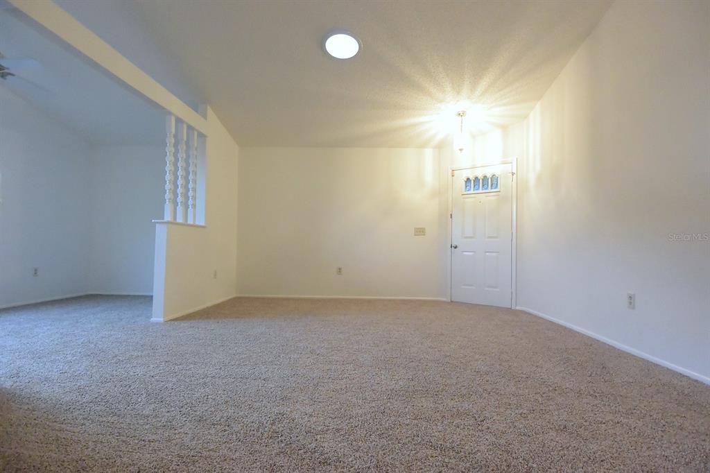 A carpeted living room features a white front door and a partial wall with spindles — 4707 WALLINGFORD COURT, NEW PORT RICHEY, FL