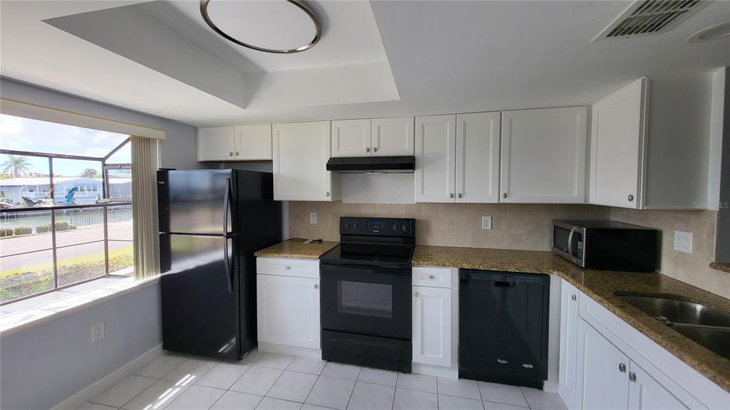 A kitchen features white cabinets, black appliances, granite countertops, and a window overlooking a canal — 19029 US HIGHWAY 19 N UNIT 23C, CLEARWATER, FL