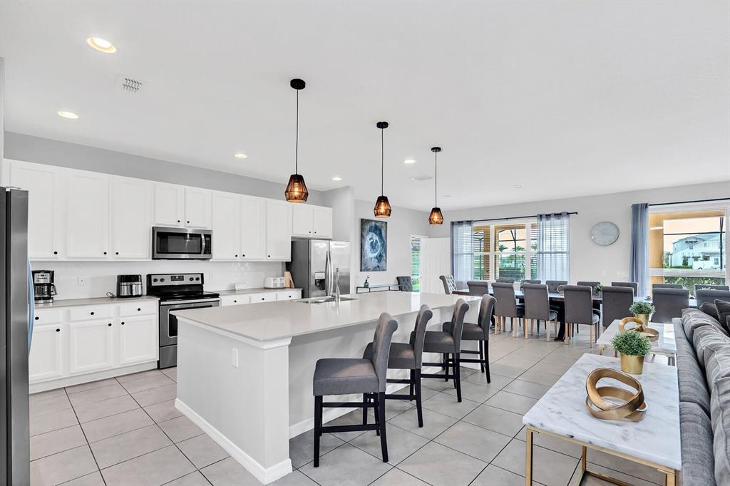 A modern kitchen features white cabinetry, a large island with bar stools, and tile flooring — 6148 BROAD OAK DRIVE, DAVENPORT, FL