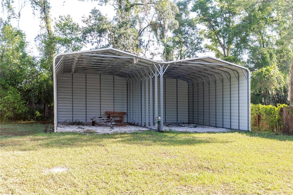 A double-bay metal carport stands in a grassy yard surrounded by trees — 13203 BLISSFIELD, ODESSA, FL