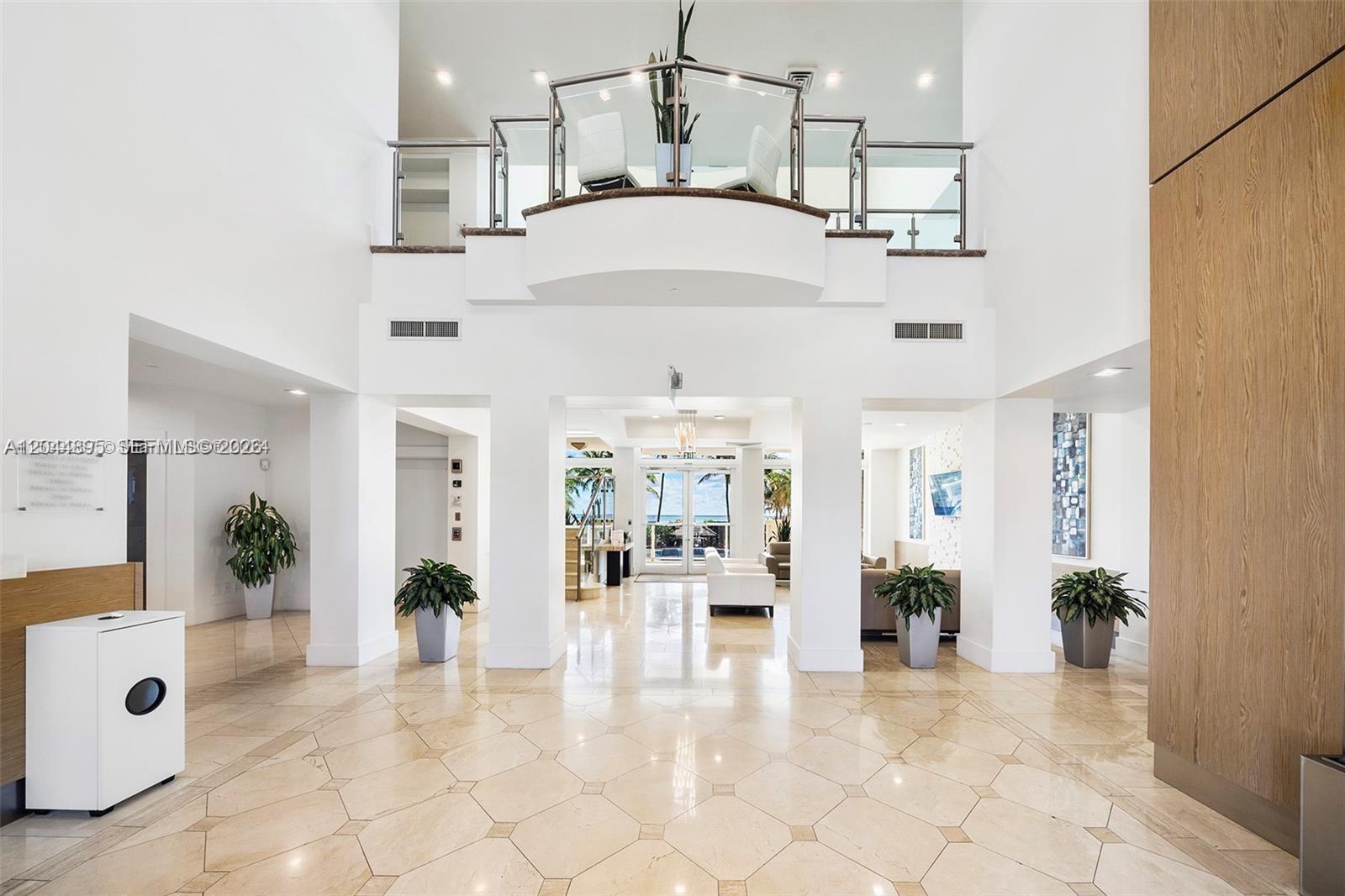 A spacious, high-ceilinged lobby features marble tile floors, white pillars, and a glass-railed mezzanine — 4779 Collins Ave # 3102, Miami Beach FL 33140, MIAMI BEACH, FL