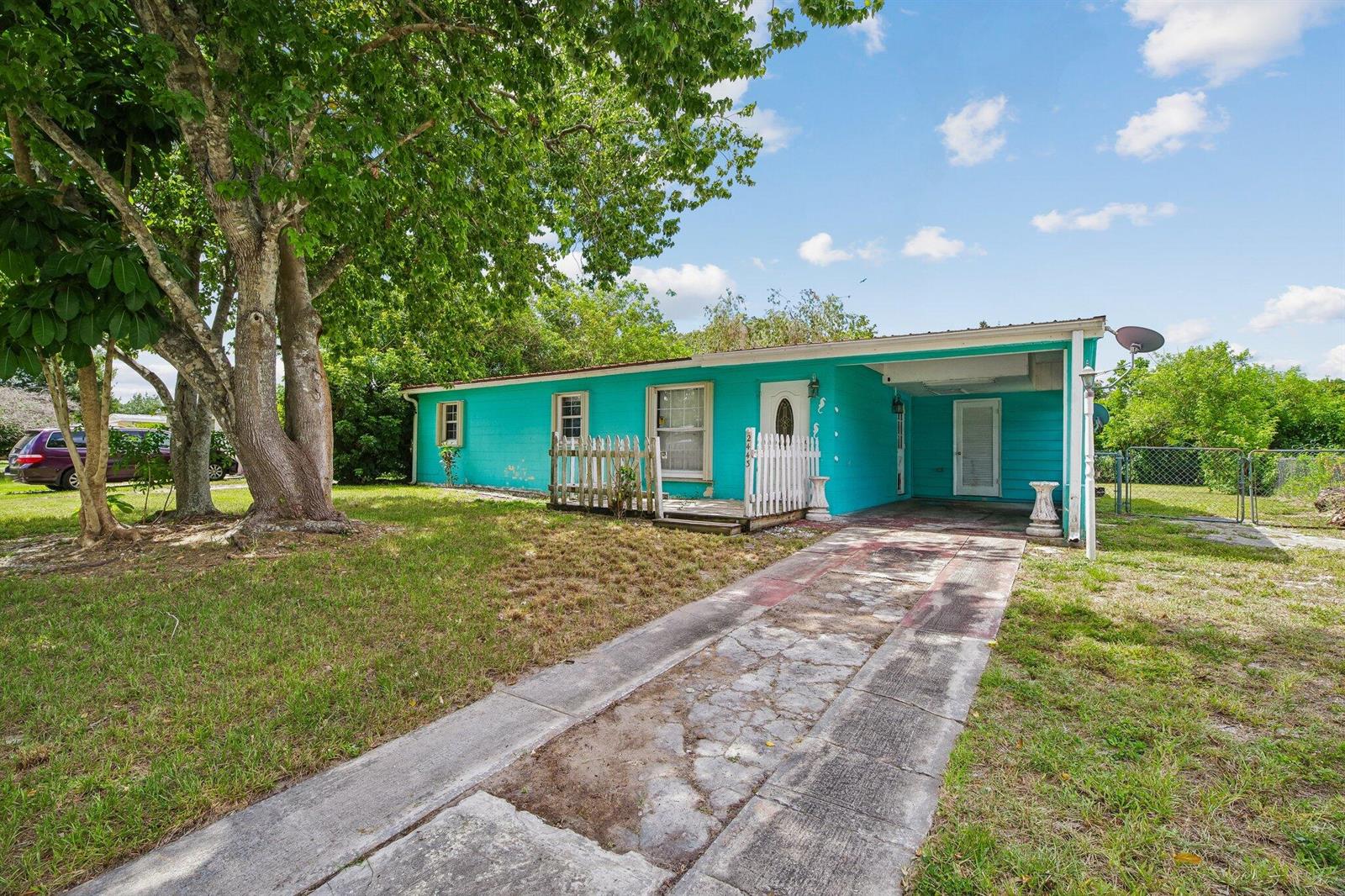 A bright teal, single-story house with a white picket fence and a concrete driveway — 2443 2nd Place SW, Vero Beach FL 32962, VERO BEACH, FL