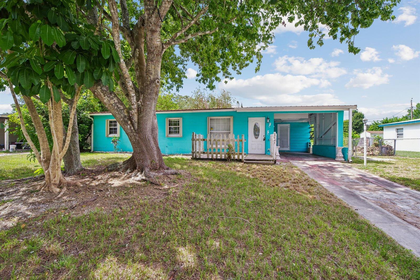 A bright turquoise single-story house features a front porch, a carport, and a large tree — 2443 2nd Place SW, Vero Beach FL 32962, VERO BEACH, FL