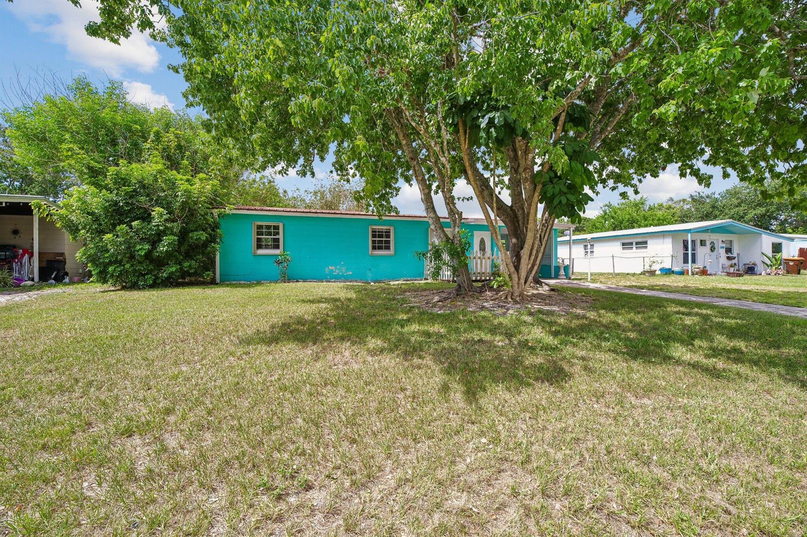 A bright turquoise single-story home sits behind a large tree on a grassy lot — 2443 2nd Place SW, Vero Beach FL 32962, VERO BEACH, FL