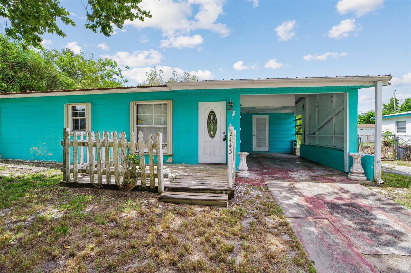 A bright turquoise single-story house features a wooden front deck and an attached carport — 2443 2nd Place SW, Vero Beach FL 32962, VERO BEACH, FL