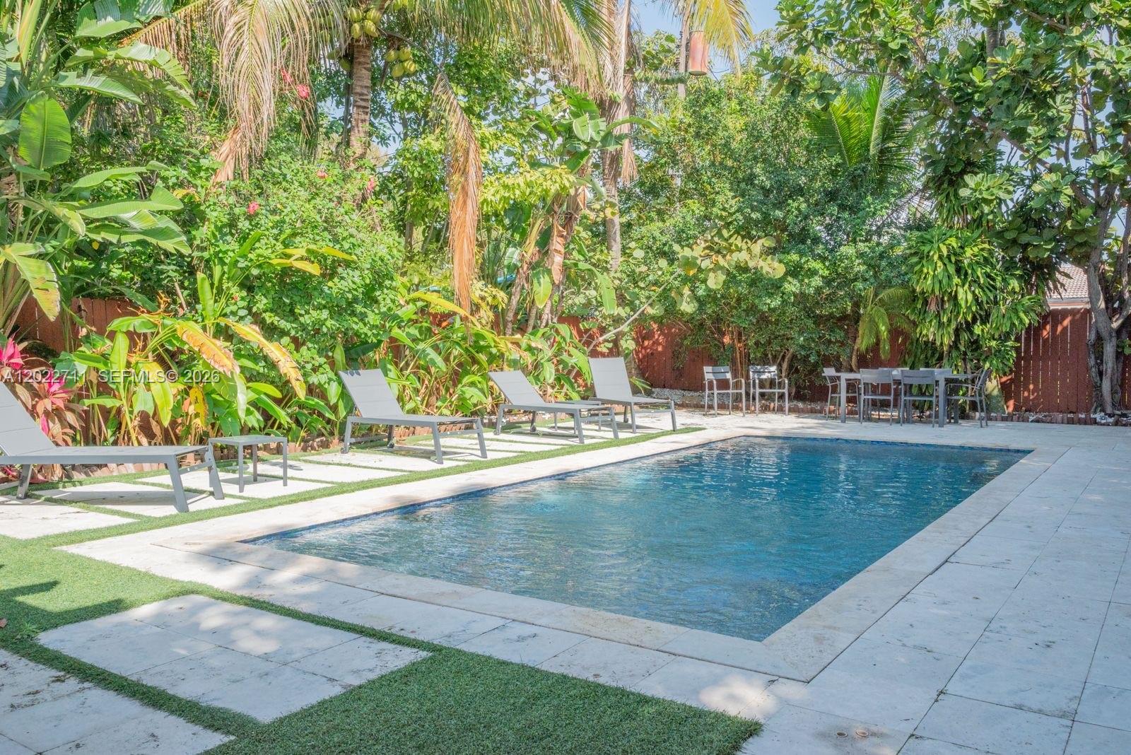 A rectangular swimming pool is surrounded by a stone patio, lounge chairs, and lush landscaping — 443 NE 71st St, Miami FL 33138, MIAMI, FL