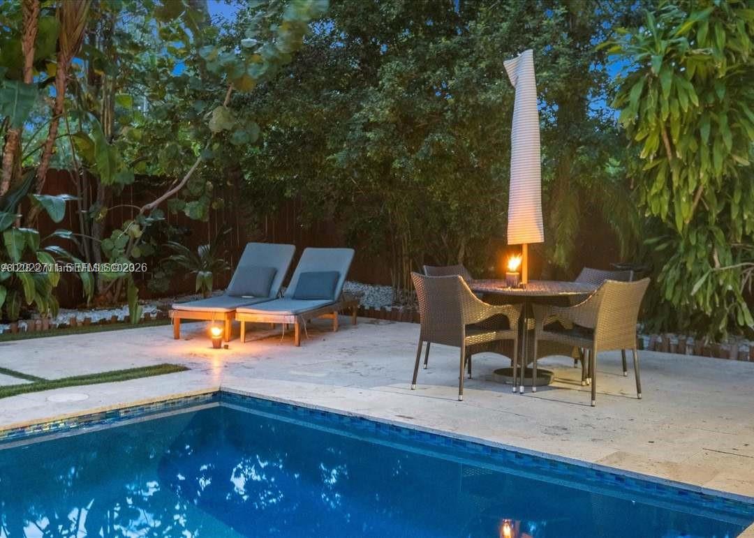 A swimming pool sits in front of a patio with lounge chairs and dining furniture — 443 NE 71st St, Miami FL 33138, MIAMI, FL