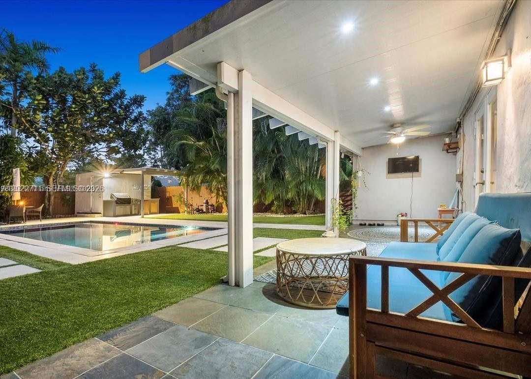 A covered patio with a blue sofa overlooks a backyard swimming pool at twilight — 443 NE 71st St, Miami FL 33138, MIAMI, FL