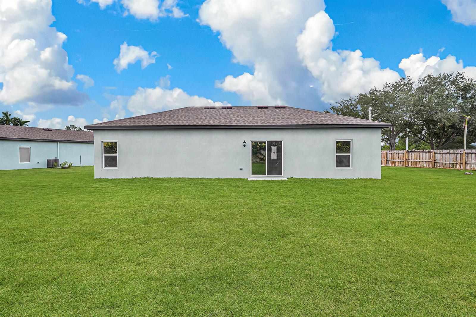 The rear exterior of a single-story house features a light-colored facade, sliding glass doors, and windows — 7855 104th Avenue, Vero Beach FL 32967, VERO BEACH, FL