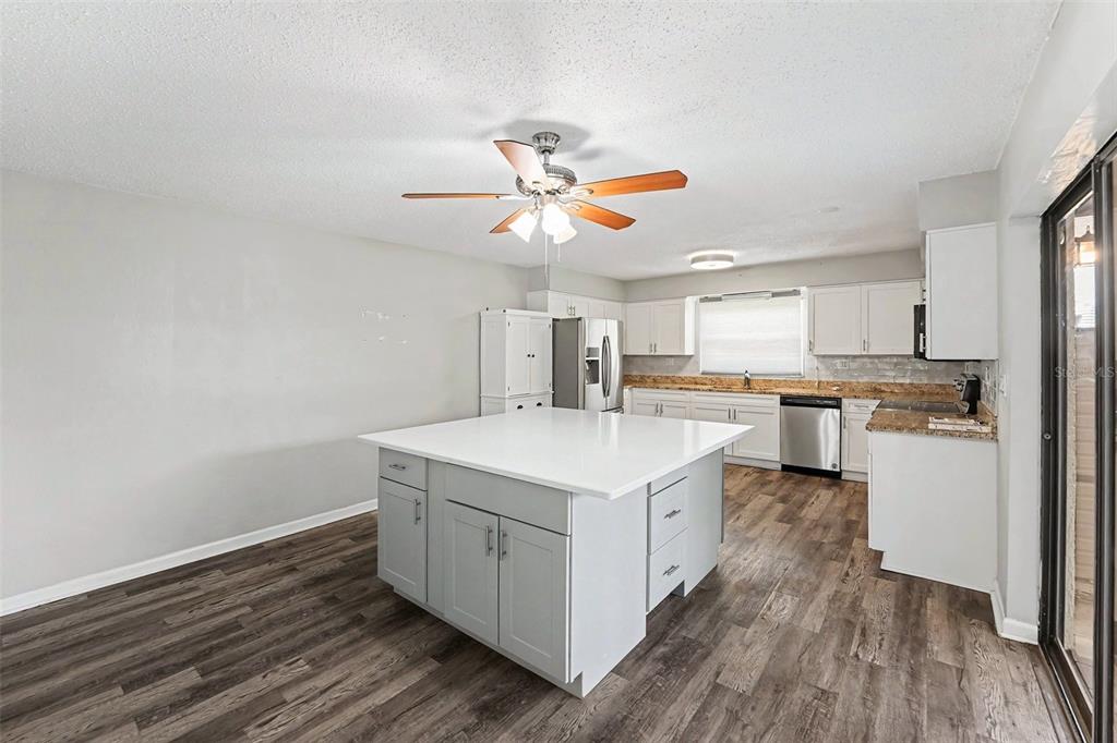 A kitchen with a large gray island, white cabinets, granite countertops, and wood-look flooring — 14521 CATALINA CIRCLE, SEMINOLE, FL