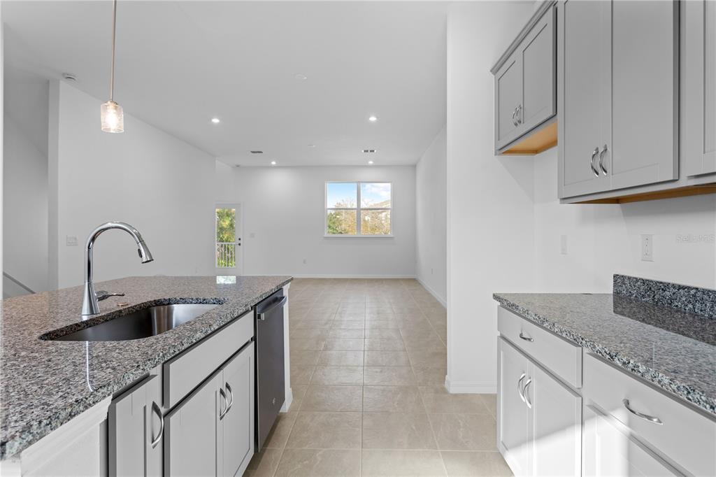A kitchen with granite countertops and gray cabinets opens into a bright, tiled living area — 9614 MONTAGUE STREET, WESTCHASE, FL