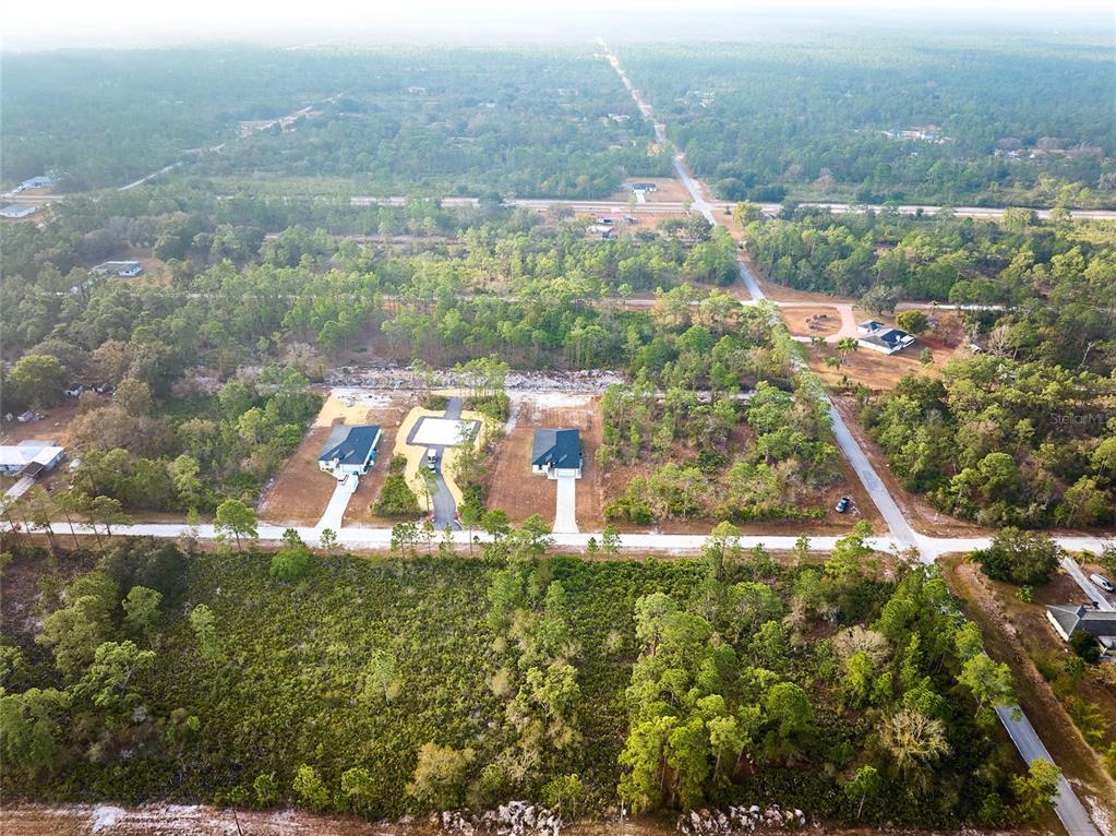 An aerial view shows three newly constructed houses situated on cleared lots amidst a wooded area — 3431 ORCHID DRIVE, INDIAN LAKE ESTATES, FL