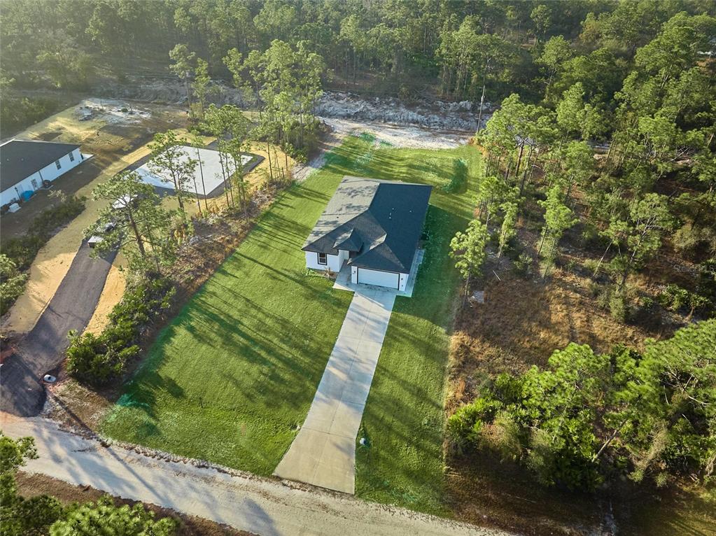 An aerial view shows a single-story house with a concrete driveway surrounded by wooded land — 3431 ORCHID DRIVE, INDIAN LAKE ESTATES, FL
