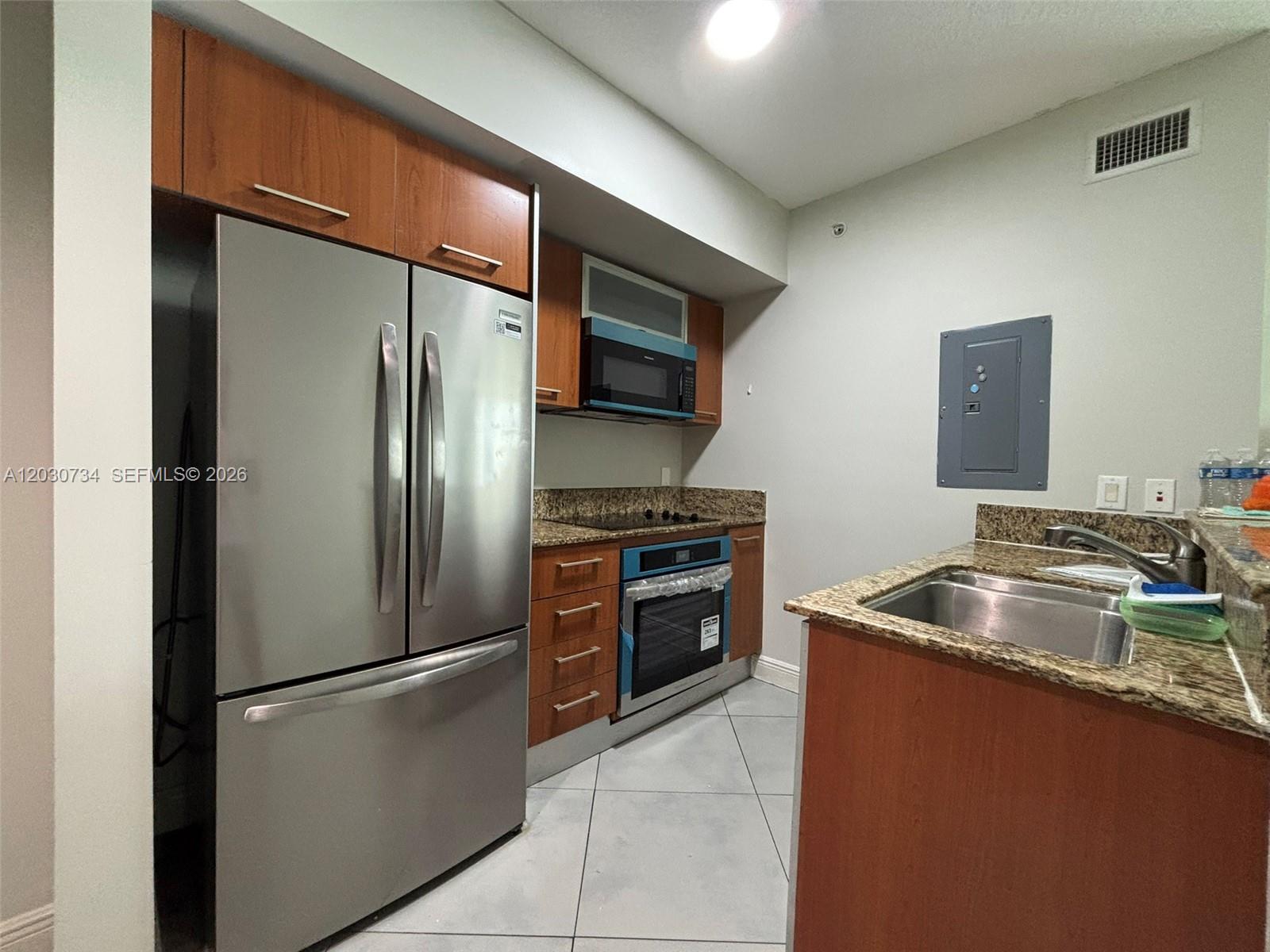 A kitchen features stainless steel appliances, wood cabinets, granite countertops, and light-colored tile flooring — 9055 SW 73rd Ct # 1504, Miami FL 33156, MIAMI, FL