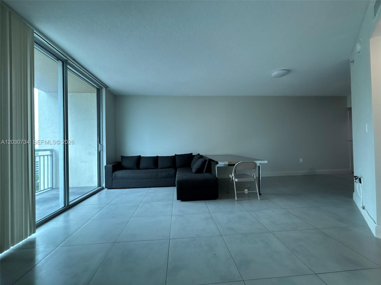 A living room features light gray tile floors, a black sectional sofa, and a balcony door — 9055 SW 73rd Ct # 1504, Miami FL 33156, MIAMI, FL