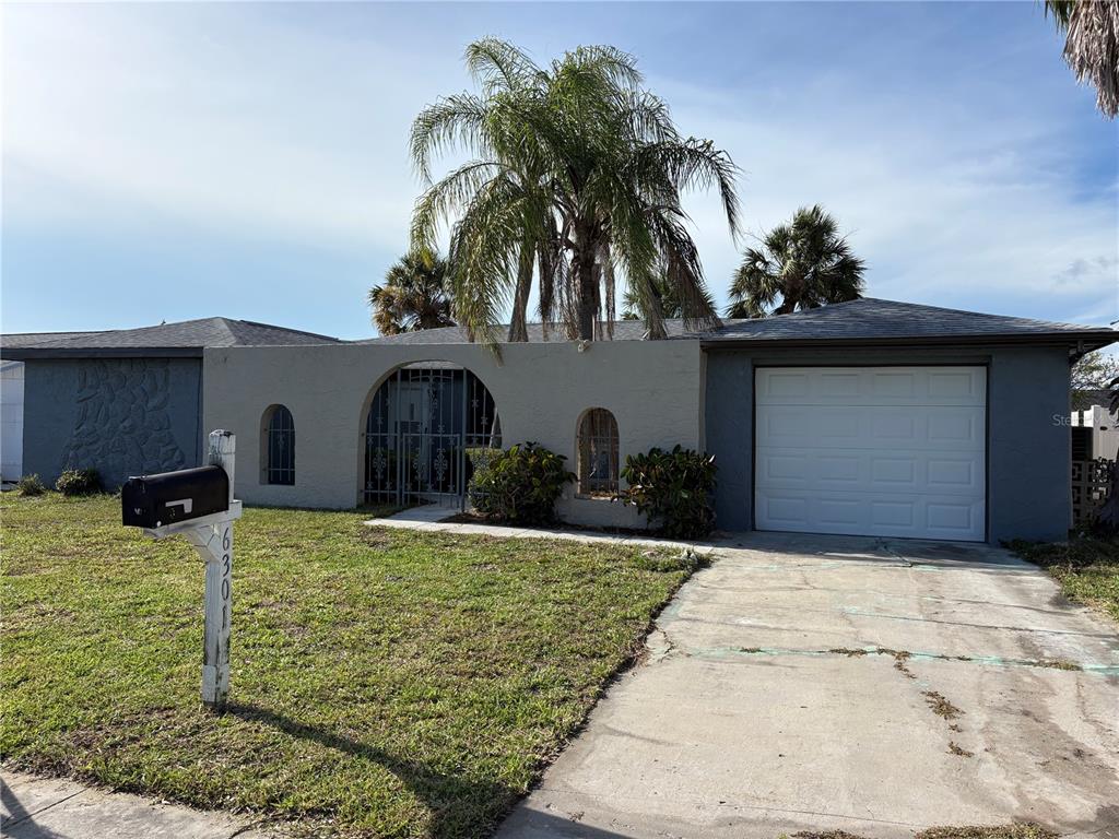 A single-story house with a gray stucco exterior, a central arched entryway, and a garage — 6301 SEABREEZE DRIVE, PORT RICHEY, FL