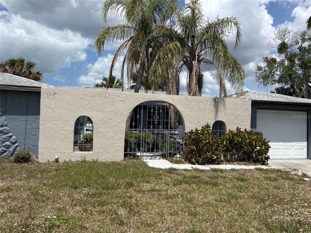 A beige stucco wall with arched openings and a metal gate stands before a house — 6301 SEABREEZE DRIVE, PORT RICHEY, FL